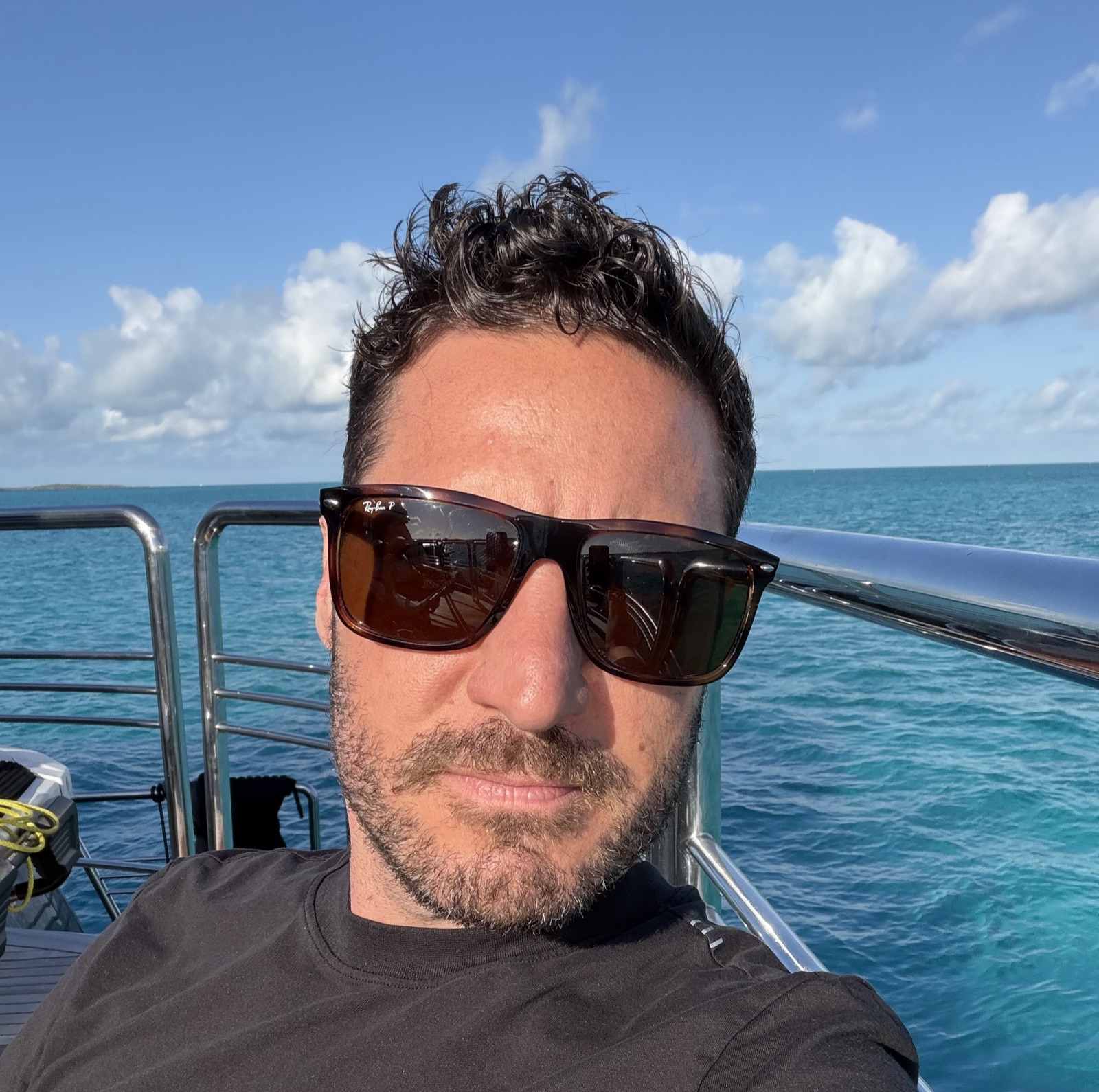 Peter wearing sunglasses on a sunny boat with bright blue sea behind him